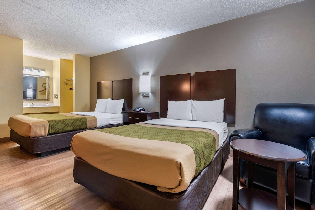 A hotel room with two beds, a small table, a chair, and a mirror.