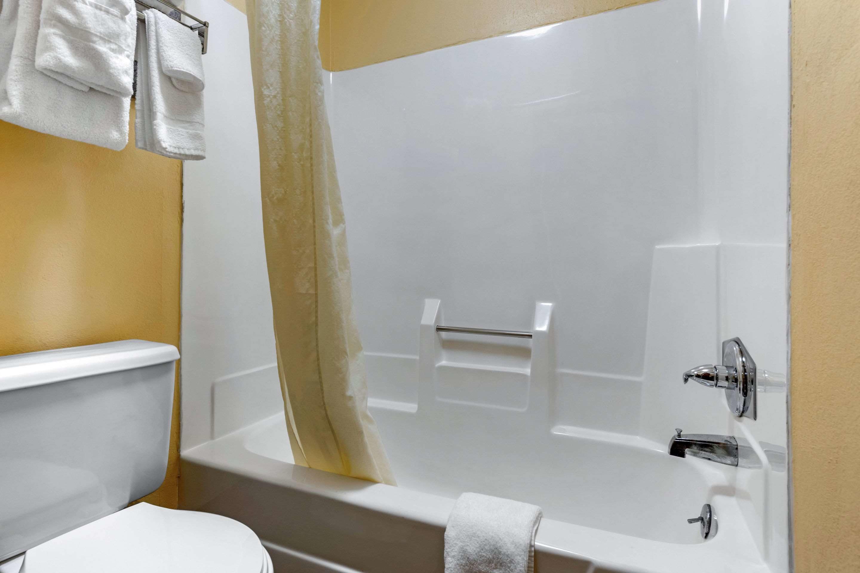 A bathroom with a white bathtub, a toilet, and a towel rack with towels.