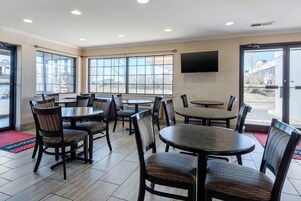 Un restaurante con varias mesas y sillas, ventanas amplias y un televisor de pantalla plana montado en la pared.