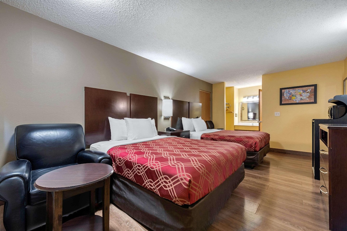 A hotel room with two beds, a desk, a chair, and a small table.