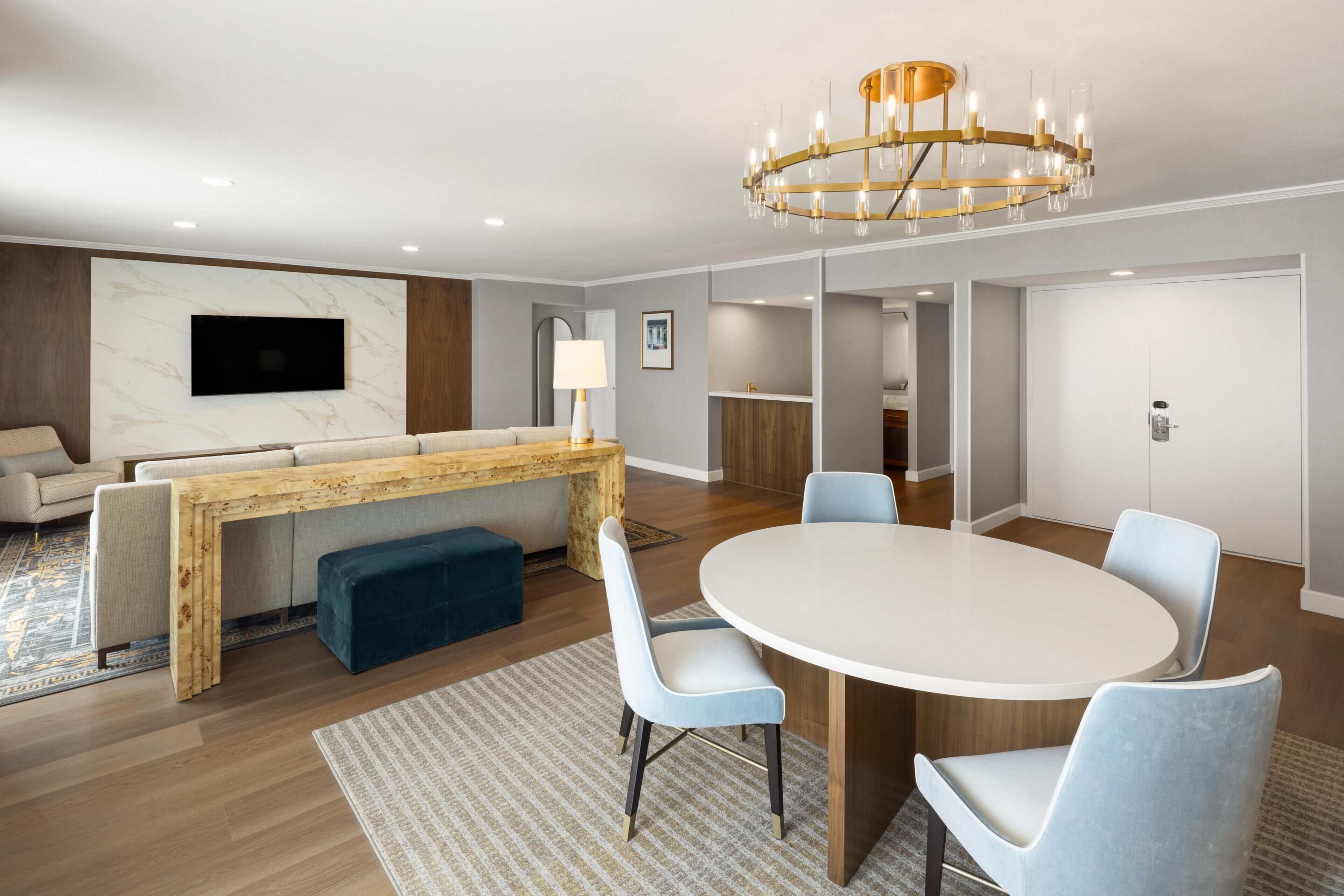 A modern living room with a wooden bench, a round table, and light blue chairs.