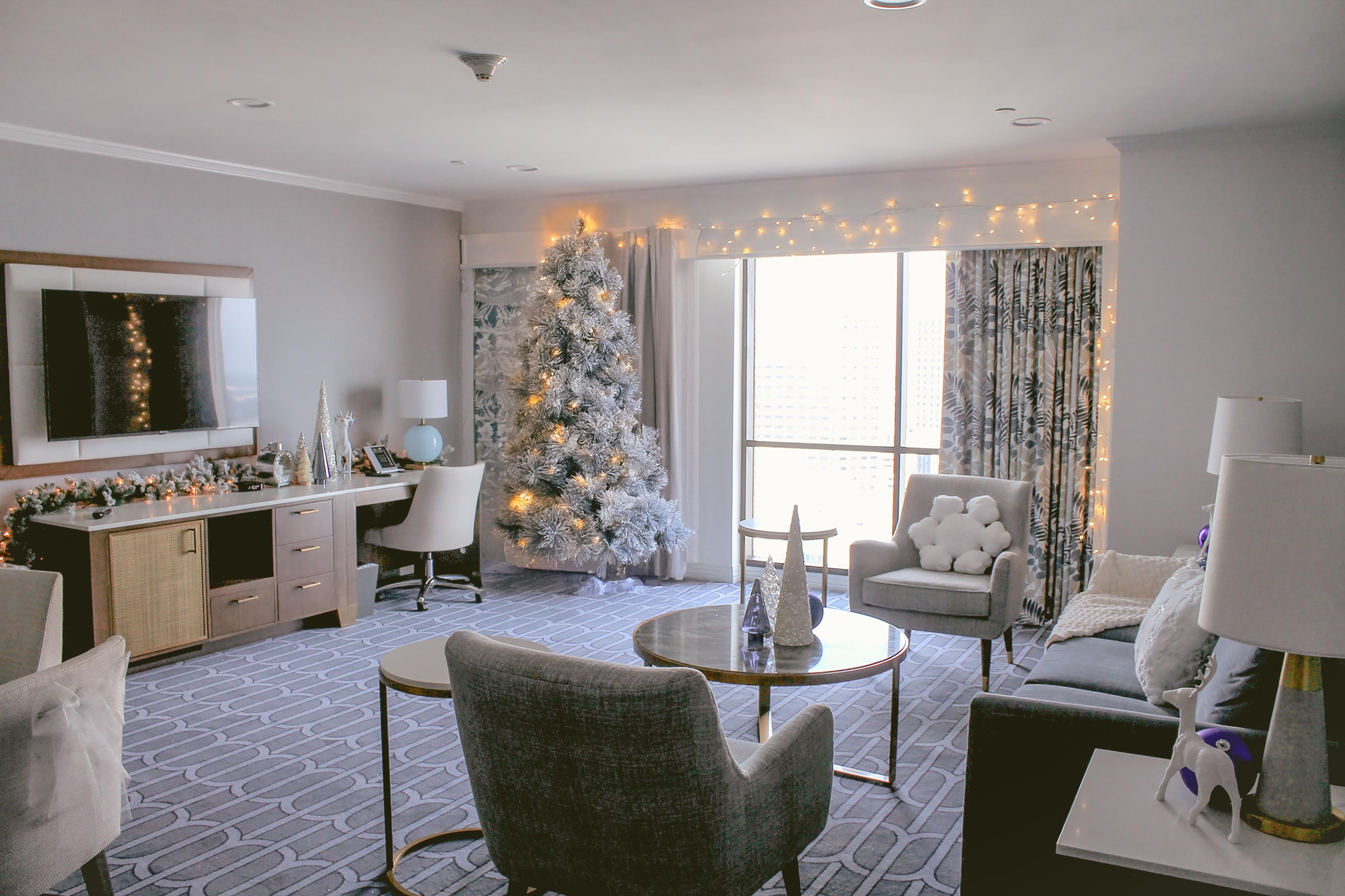 Una habitación de hotel moderna con un gran árbol de Navidad, un televisor de pantalla plana, un comedor y vistas a la ciudad.