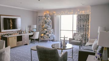 Una habitación de hotel moderna con un gran árbol de Navidad, un televisor de pantalla plana, un comedor y vistas a la ciudad.