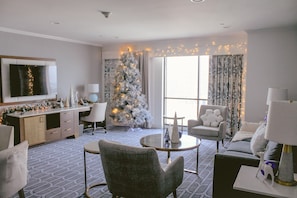 A modern hotel room with a large Christmas tree, a flat-screen TV, a dining area, and a view of the city. - Hilton New Orleans Riverside (New Orleans)