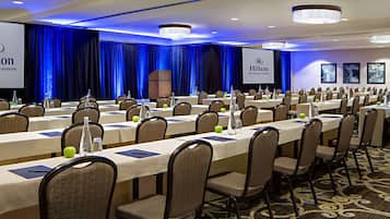 A conference room with long tables, chairs, and a screen displaying the Hilton logo.