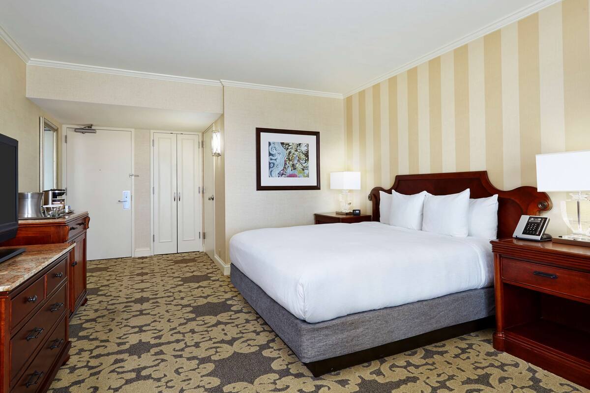 Habitación de hotel con cama, televisor, escritorio, lámpara y un cuadro en la pared.