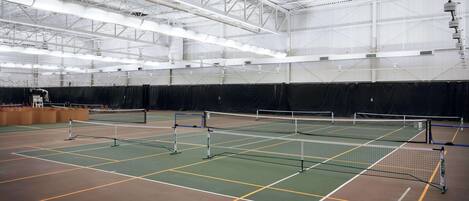 Una cancha de tenis cubierta con varias canchas, techos altos y un amplio espacio abierto.