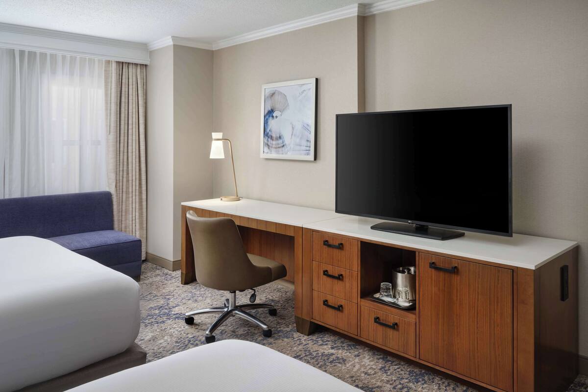 Habitación de hotel con cama, escritorio con televisor, silla, lámpara y un cuadro en la pared.