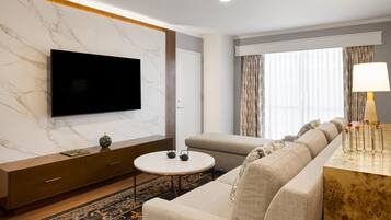 A modern hotel room with a flat-screen TV, a sofa, a small round table, and a lamp.
