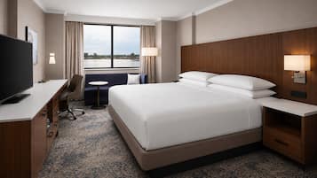 A hotel room with a large bed, a desk with a flat-screen TV, a chair, a small table, and a window with curtains.