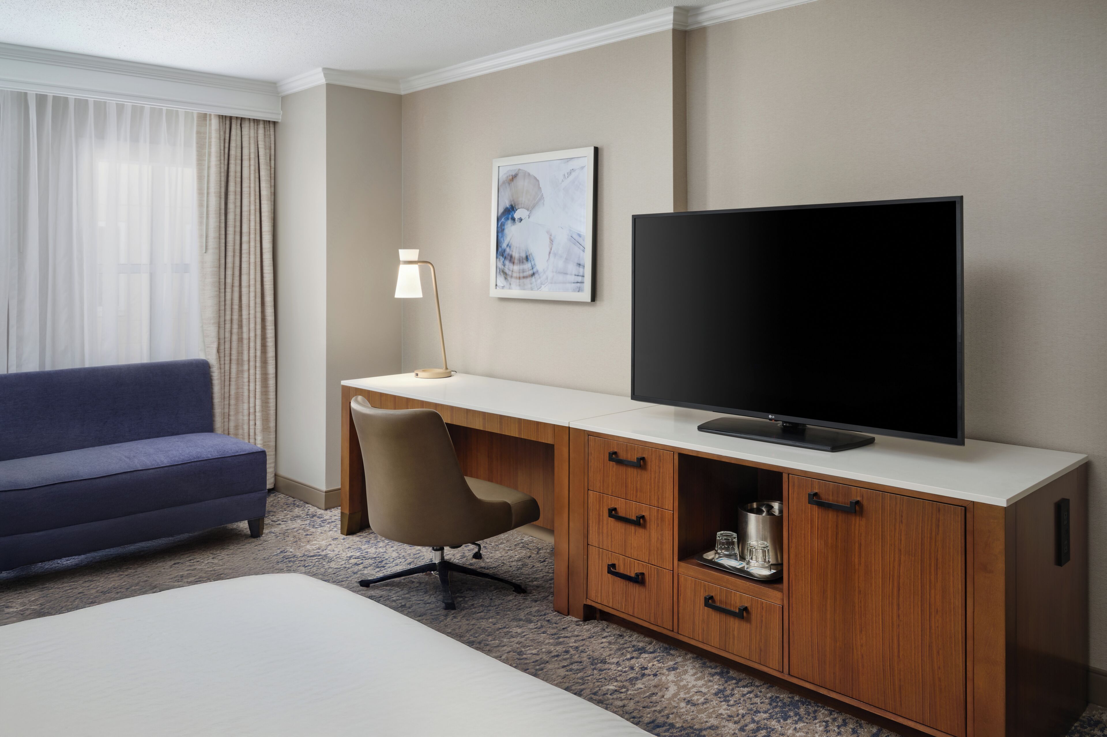A hotel room with a bed, a blue sofa, a wooden desk with a television, a chair, and a lamp.
