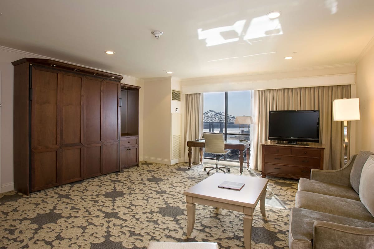 Habitación de hotel con un armario amplio, un televisor de pantalla plana, un sofá, una mesa de centro y vistas a un puente por la ventana.