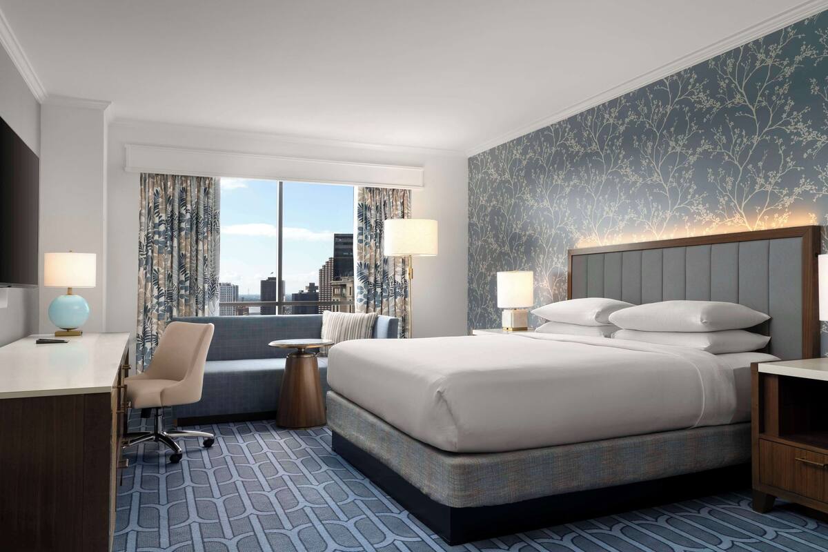 Habitación de hotel con una cama grande, un escritorio, una silla, una mesa redonda y vistas a la ciudad.
