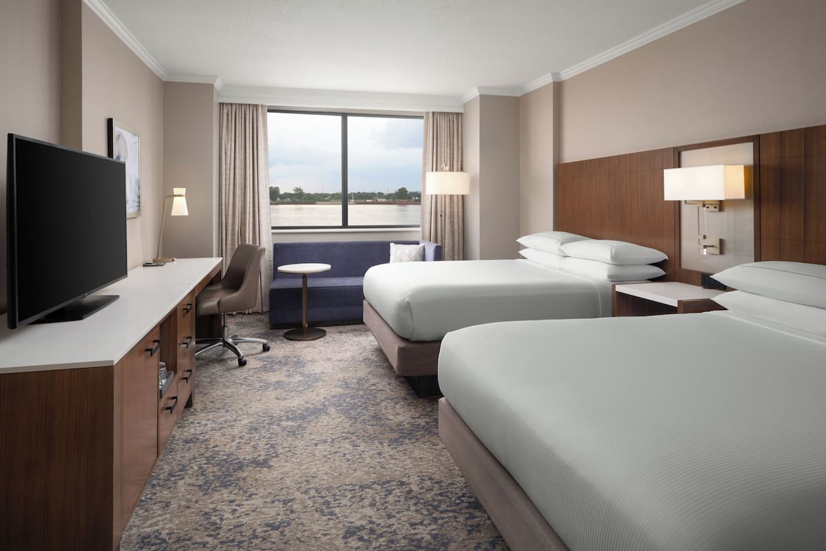 Een hotelkamer met een televisie, bureau, twee bedden, een stoel, een klein tafeltje en uitzicht op het omliggende landschap.