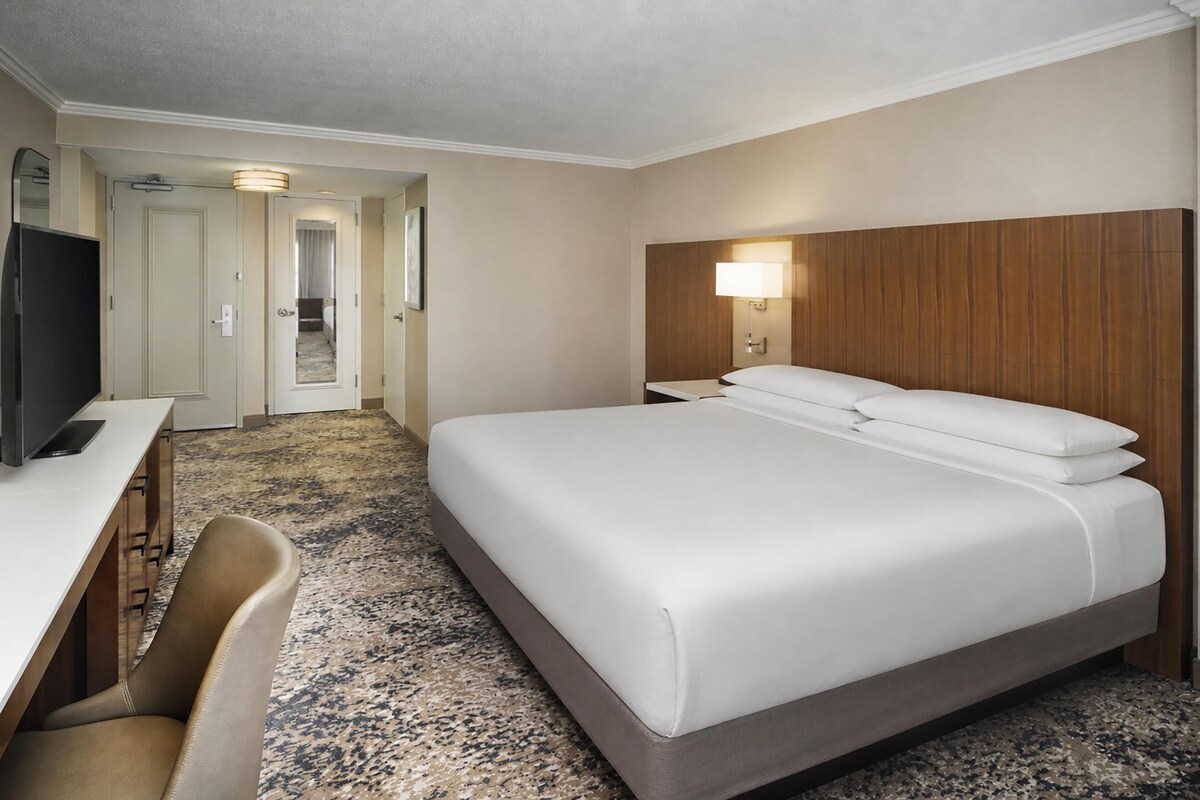 Habitación de hotel con cama, escritorio, silla, televisión y lámpara.