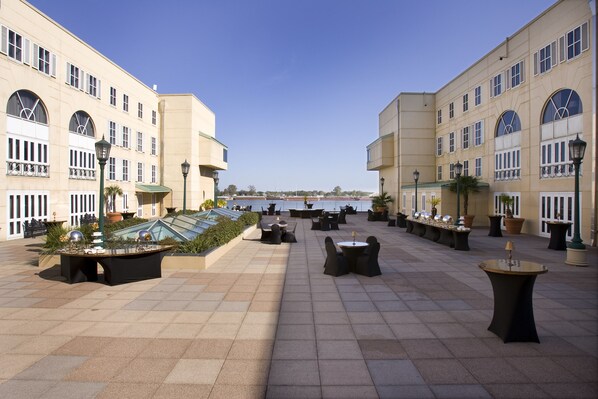 A spacious outdoor patio with multiple tables and chairs, a glass-roofed area, and a view of the sea. - Hilton New Orleans Riverside (New Orleans)