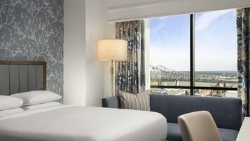 A hotel room with a large bed, a seating area, a lamp, and a view of a bridge.