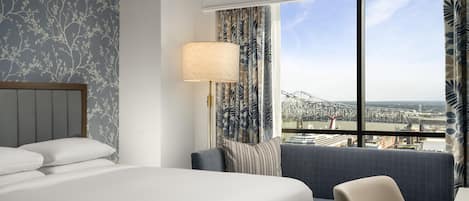 A hotel room with a large bed, a seating area, a lamp, and a view of a bridge.