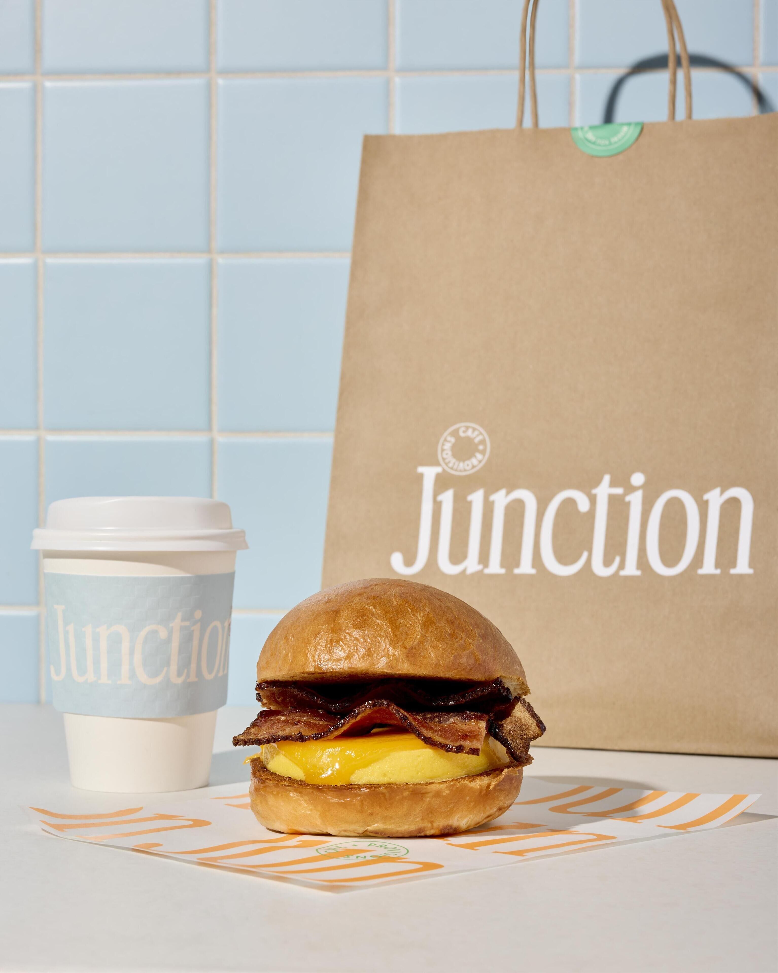 A sandwich on a table with a paper bag and a coffee cup.