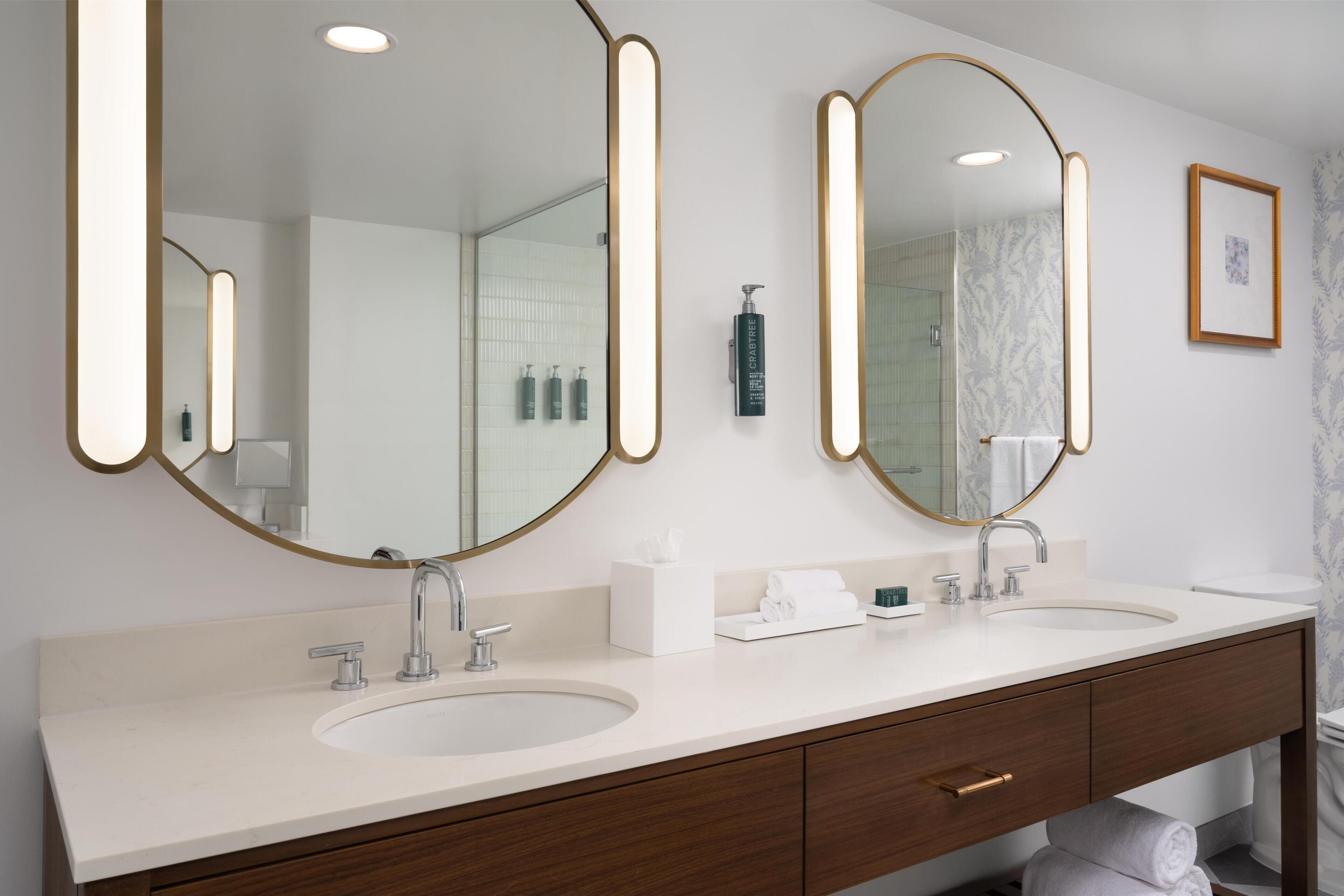 A modern bathroom with two sinks, large mirrors, and a vanity with a wooden cabinet.