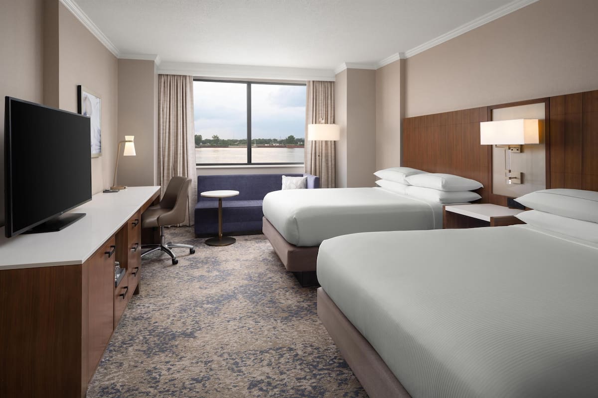 Habitación de hotel con una cama grande, televisión, escritorio, silla y vista al agua.