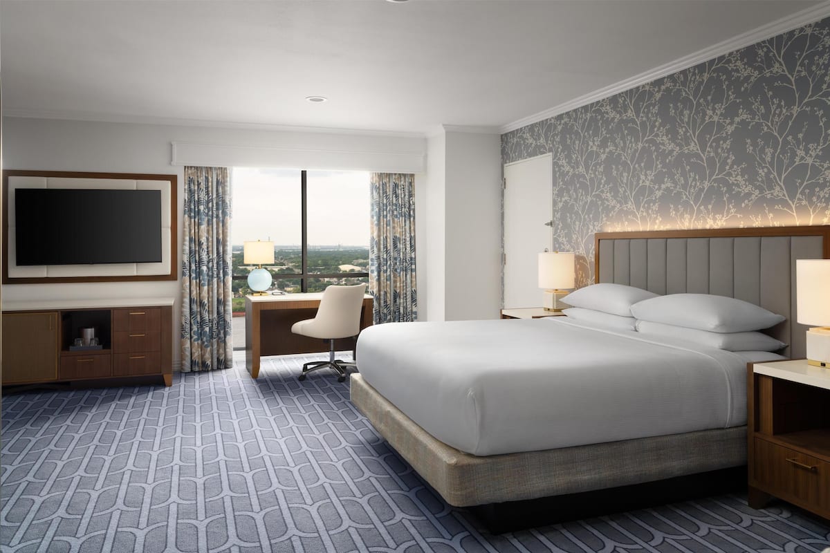 Habitación de hotel con una cama grande, un escritorio, una silla, un televisor y vistas a la ciudad.