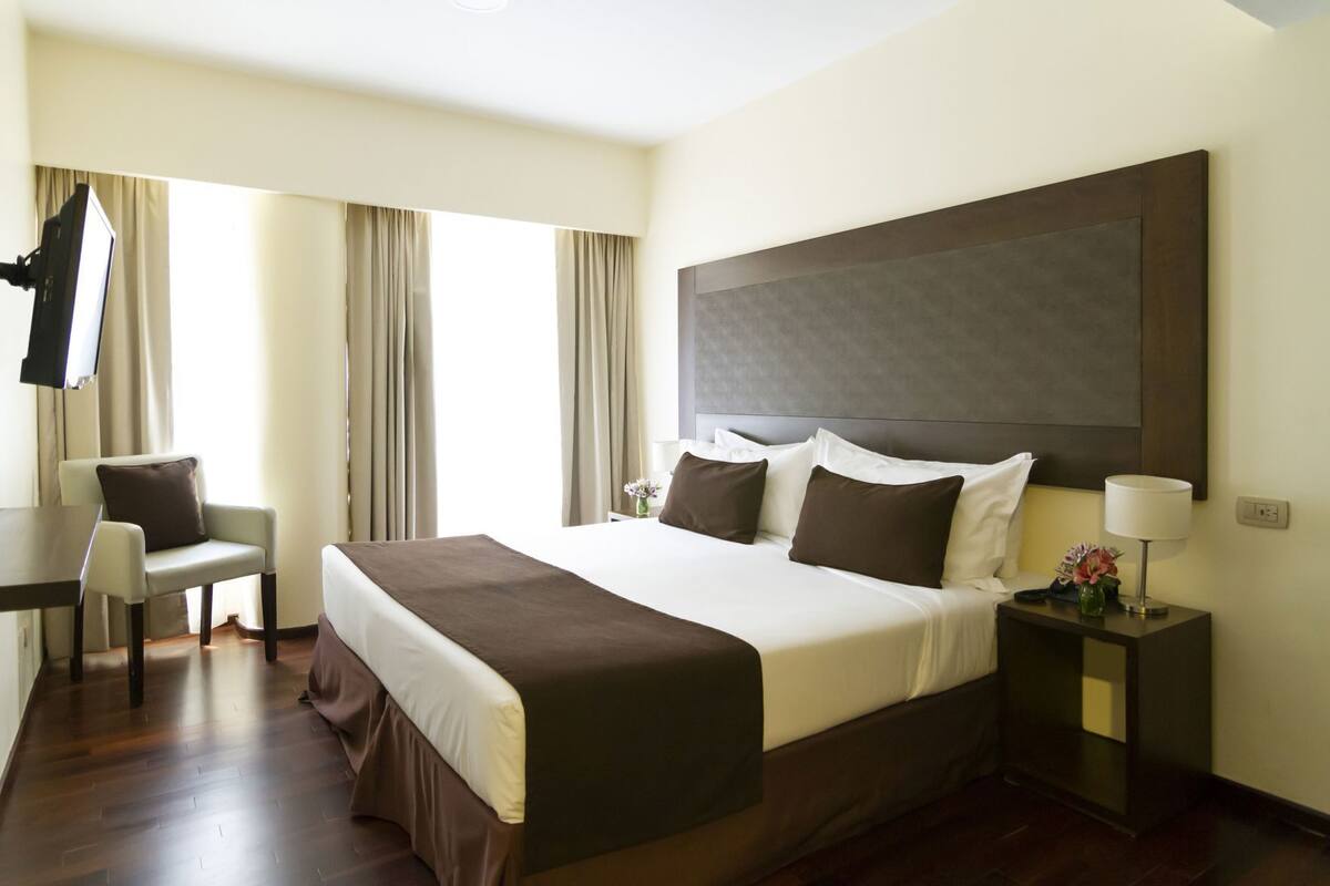 Ein Hotelzimmer mit einem großen Bett, einem Schreibtisch, einem Sessel und einem Fernseher.