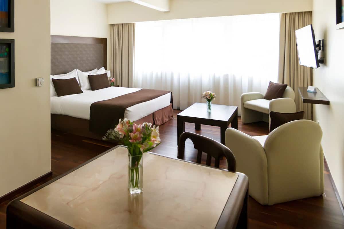 Habitación de hotel con cama, escritorio, dos sillas, televisor y ventana con cortinas.