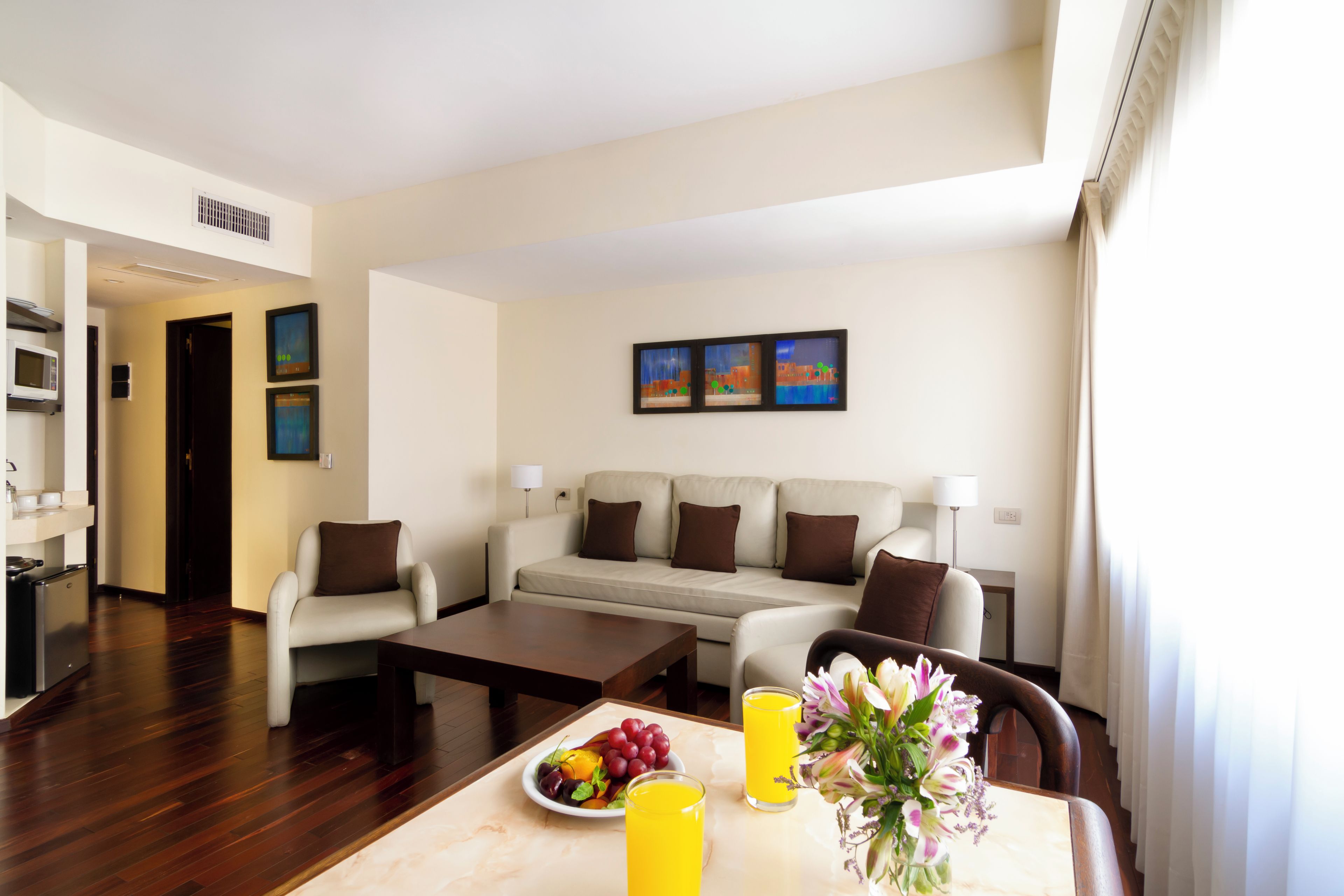 Una sala de estar moderna con un sofá, sillones, una mesa de centro y un comedor con fruta y bebidas.