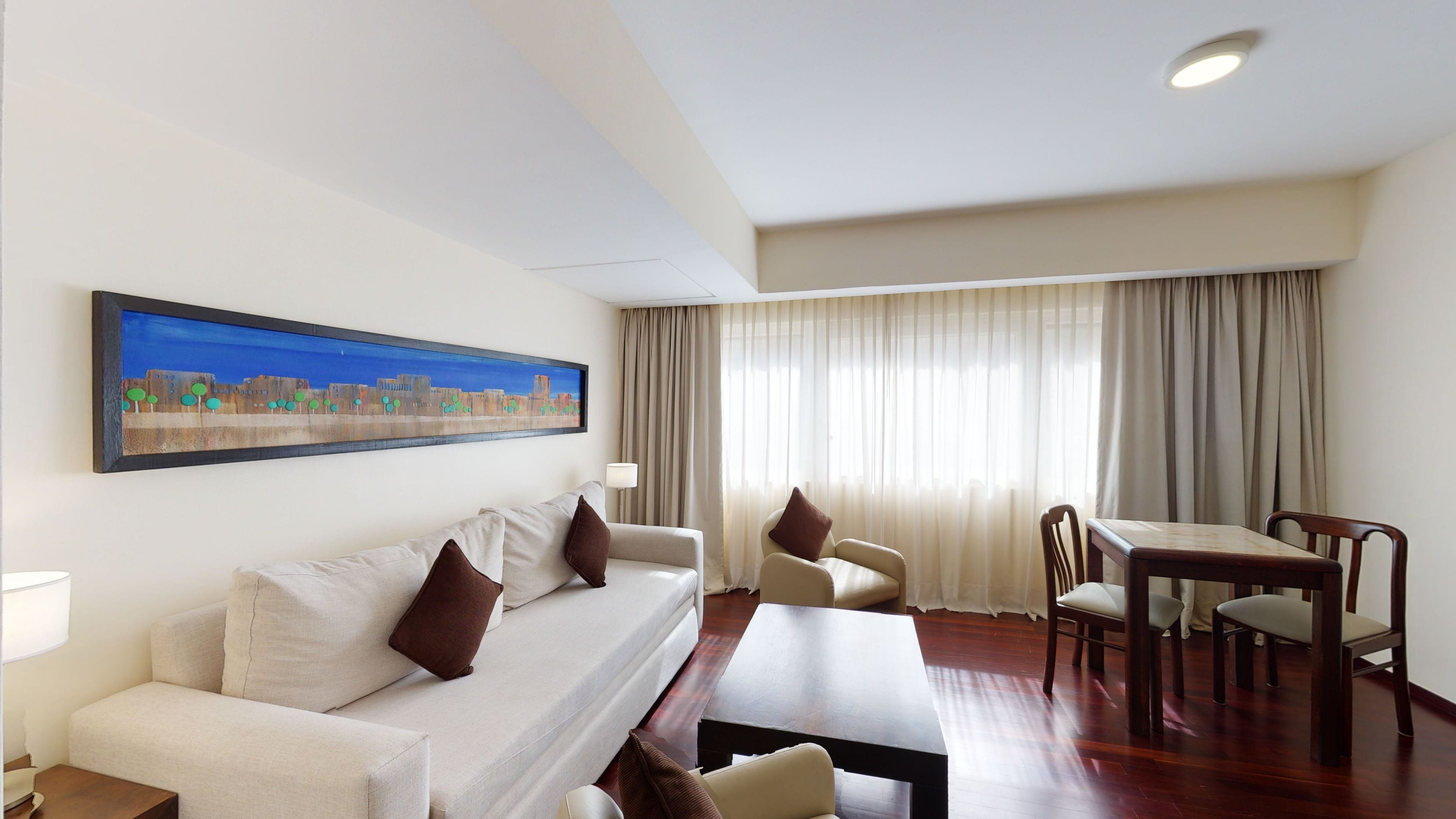 Una habitación de hotel con sofá, una mesa de comedor y un cuadro en la pared.