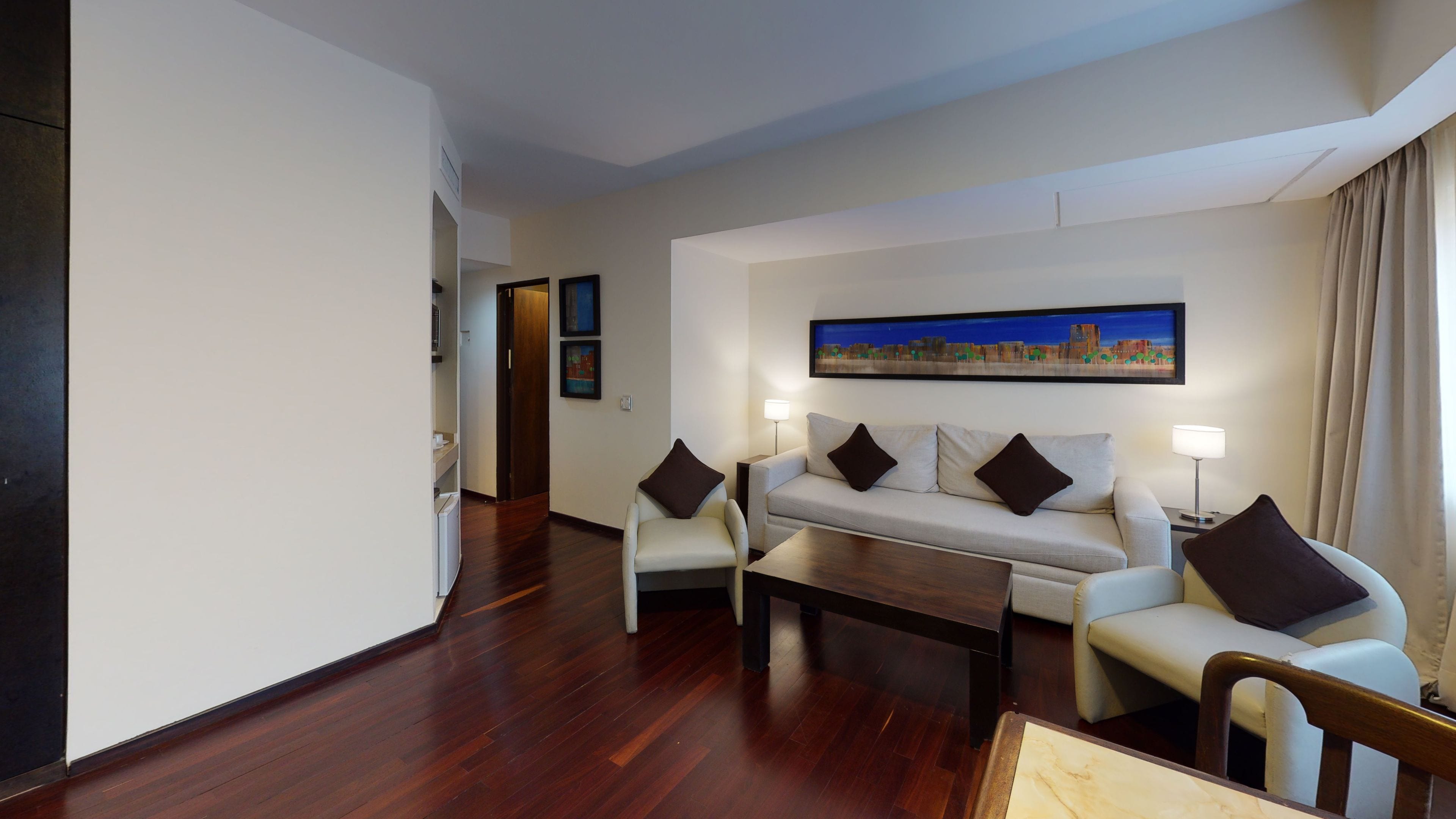 A hotel room with a sofa set, a coffee table, and a painting on the wall.