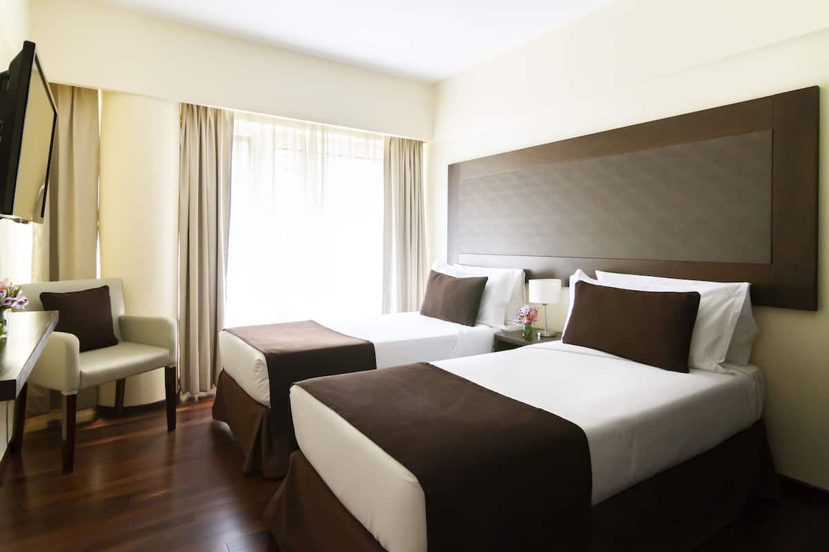 Habitación de hotel con dos camas, un escritorio, una silla y un ventanal con cortinas.