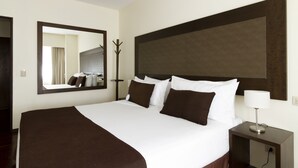 Een hotelkamer met een groot bed, een nachtkastje met een lamp, een spiegel en een kapstok.