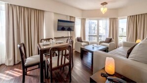 Une chambre d’hôtel équipée d’une table à manger, de deux canapés, d’un téléviseur fixé au mur et d’une grande fenêtre avec des rideaux.