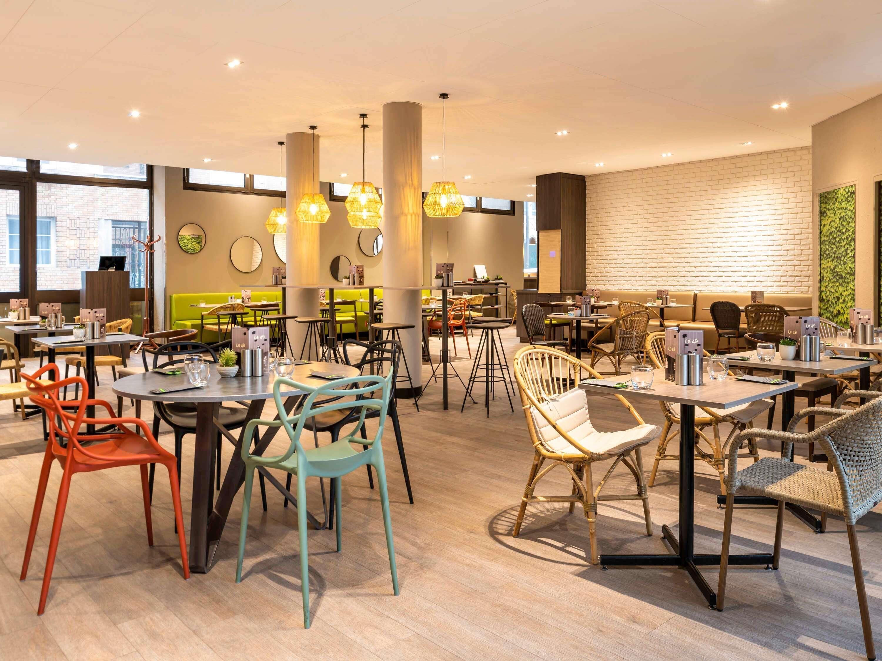 Un restaurant moderne doté de plusieurs espaces de restauration, comprenant des tables et des chaises, ainsi qu’un mur en briques agrémenté d’une plante verte.