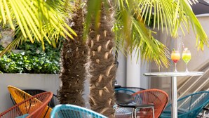 A patio area with colorful chairs, a table with drinks, and a palm tree. - ibis Paris Alésia Montparnasse 14ème (Paris)