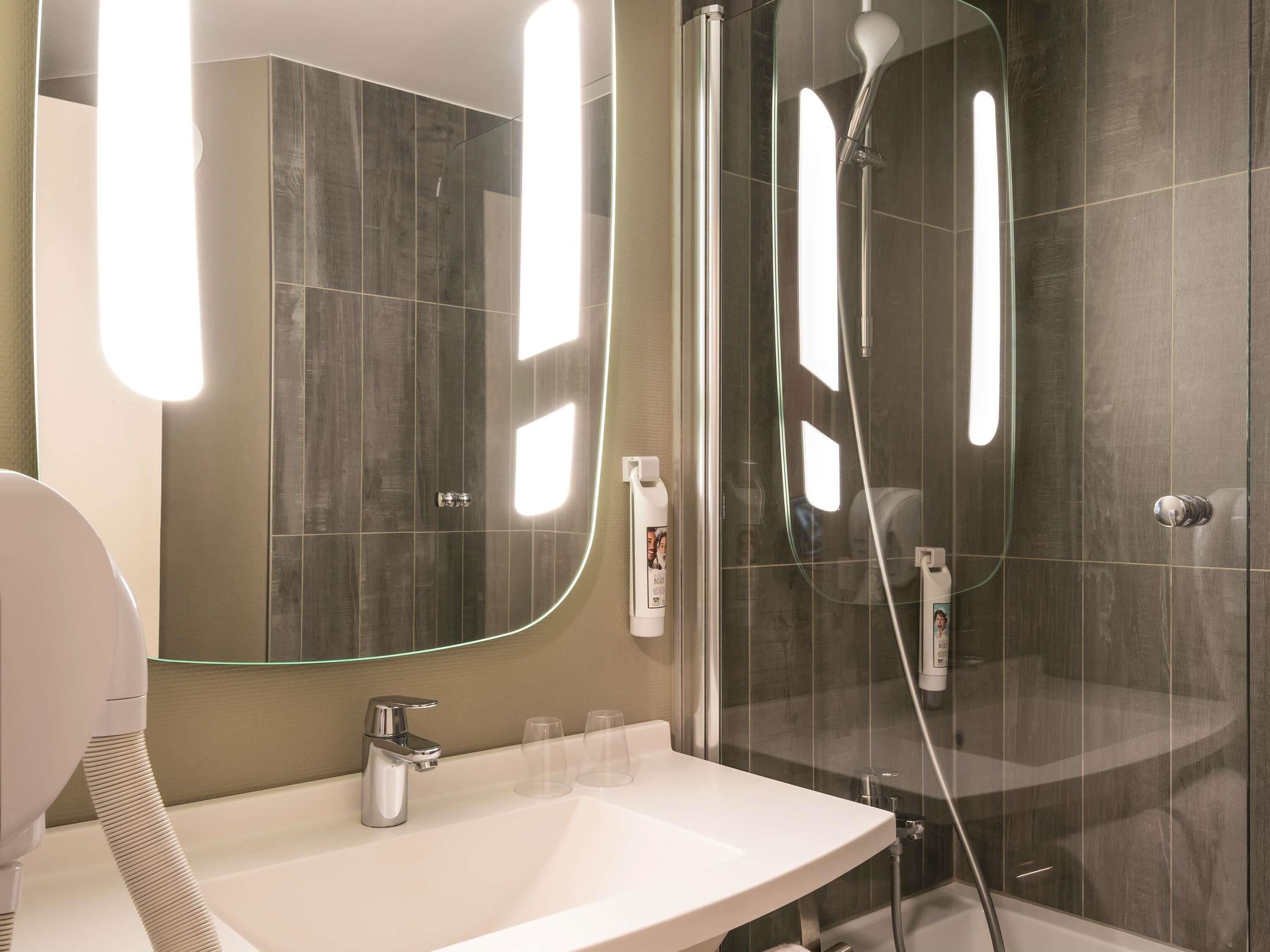 Un baño moderno con ducha de vidrio, un espejo grande y un lavamanos con dos vasos.
