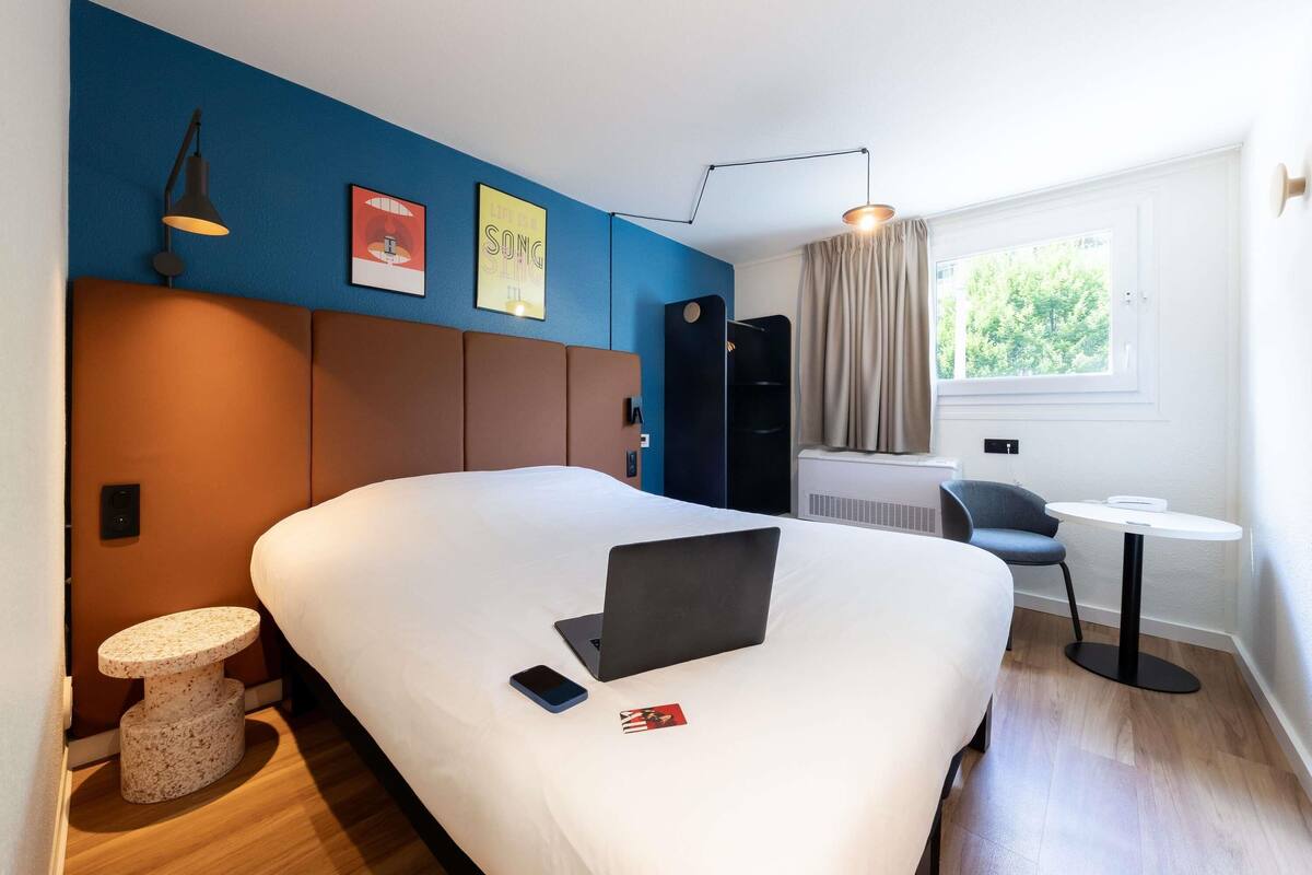 Una habitación de hotel moderna con una cama grande, un escritorio, una computadora portátil y una pequeña mesa redonda.