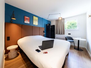 Una habitación de hotel moderna con una cama grande, un escritorio, una computadora portátil y una pequeña mesa redonda.