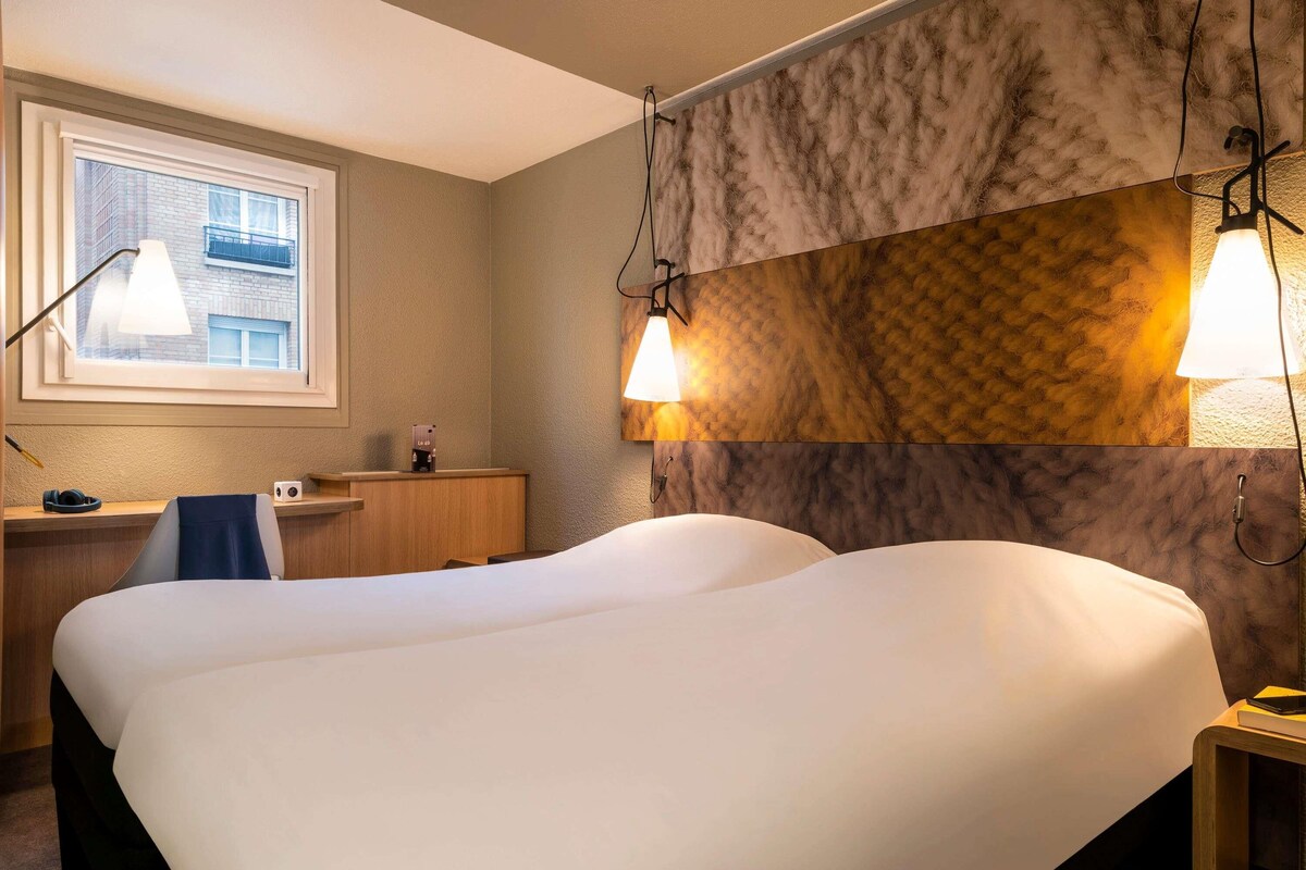 Camera d'albergo con un letto grande, una scrivania, una sedia e una finestra con vista sugli edifici.