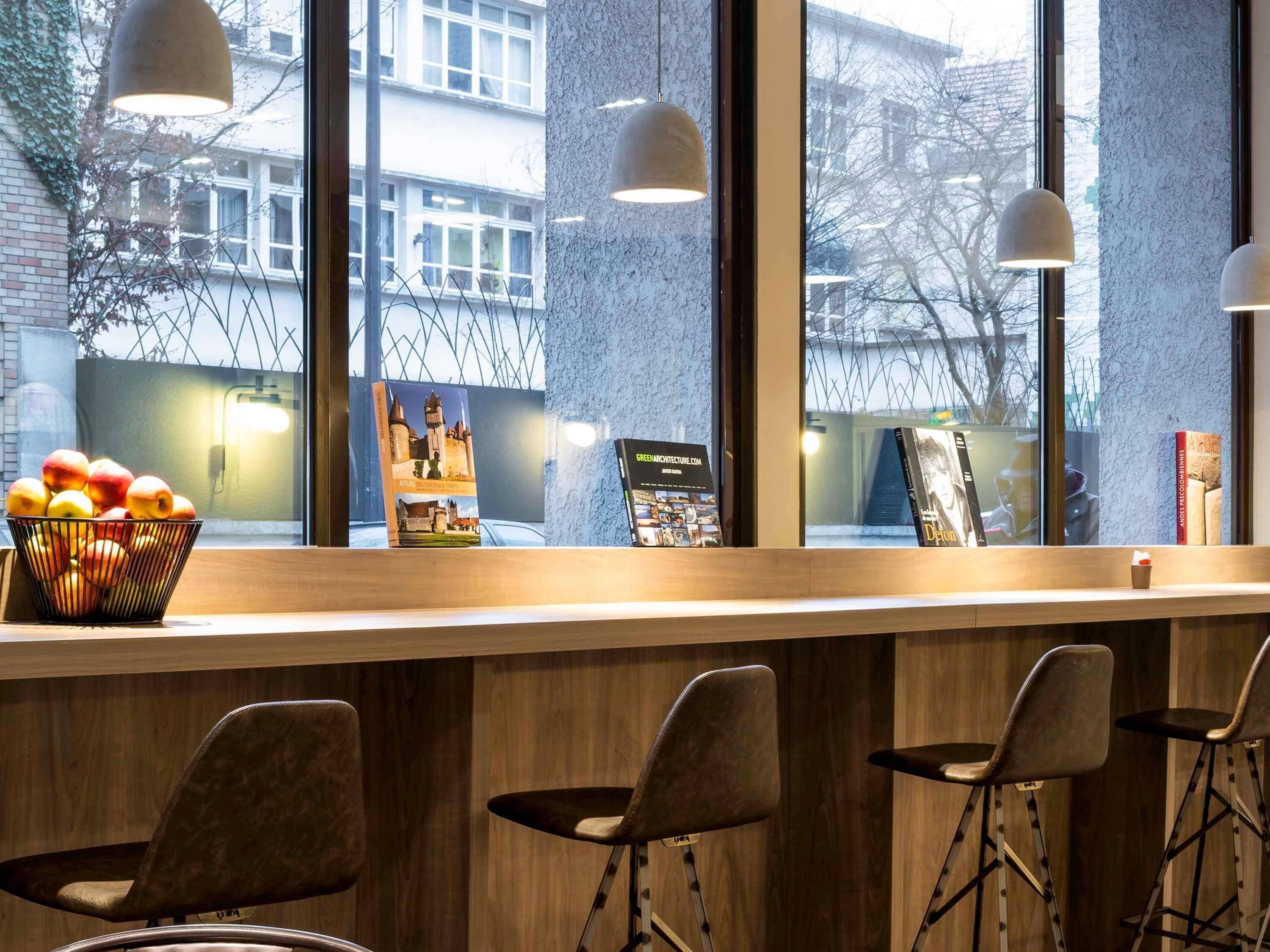 A bar area with a wooden counter, bar stools, and a window with a view of buildings and bare trees.