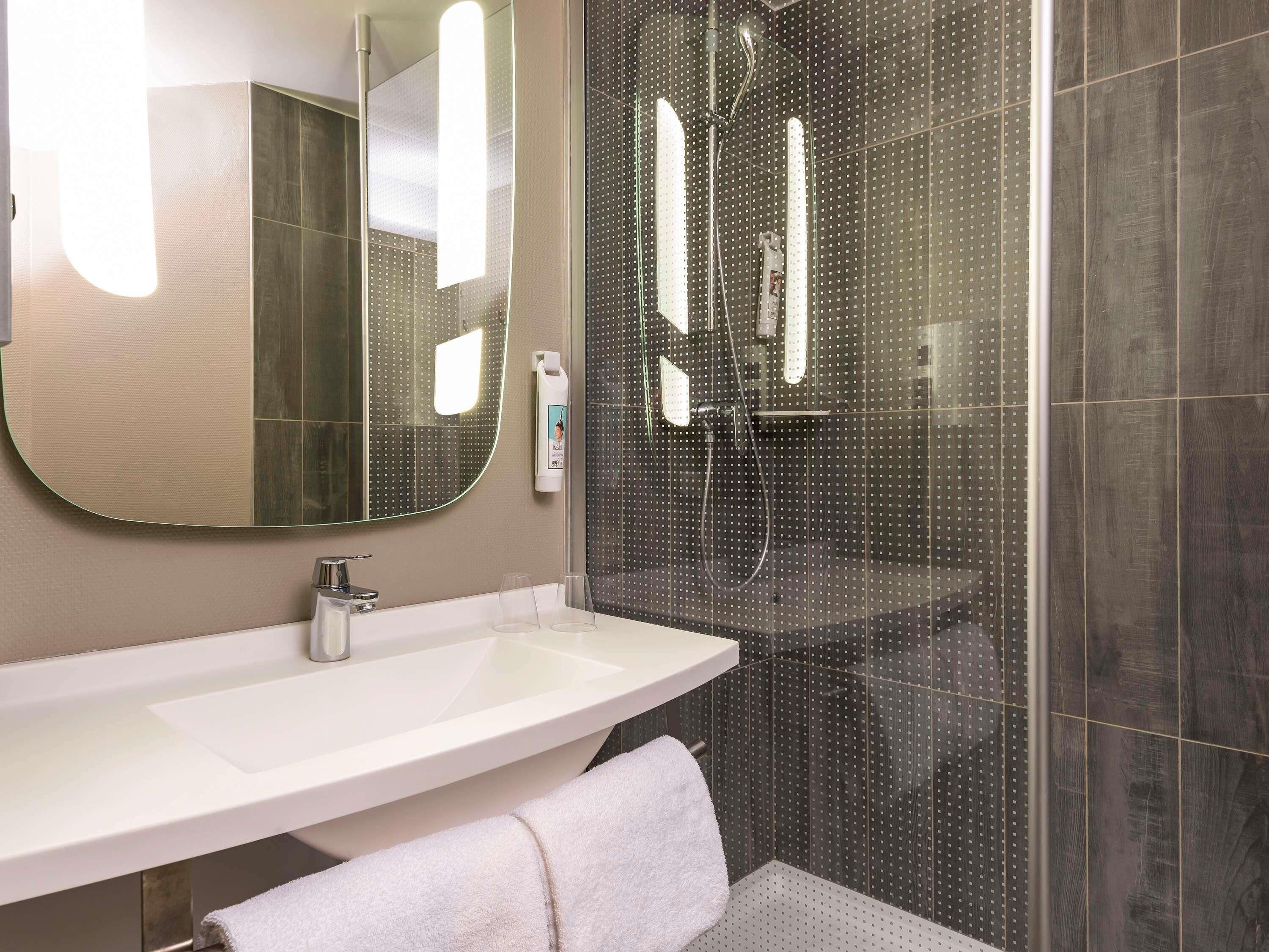 A modern bathroom with a large mirror, a sink, and a shower enclosure.