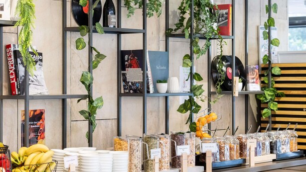 A counter with various food items and a wall decorated with plants and books. - ibis Paris Alésia Montparnasse 14ème (Paris)