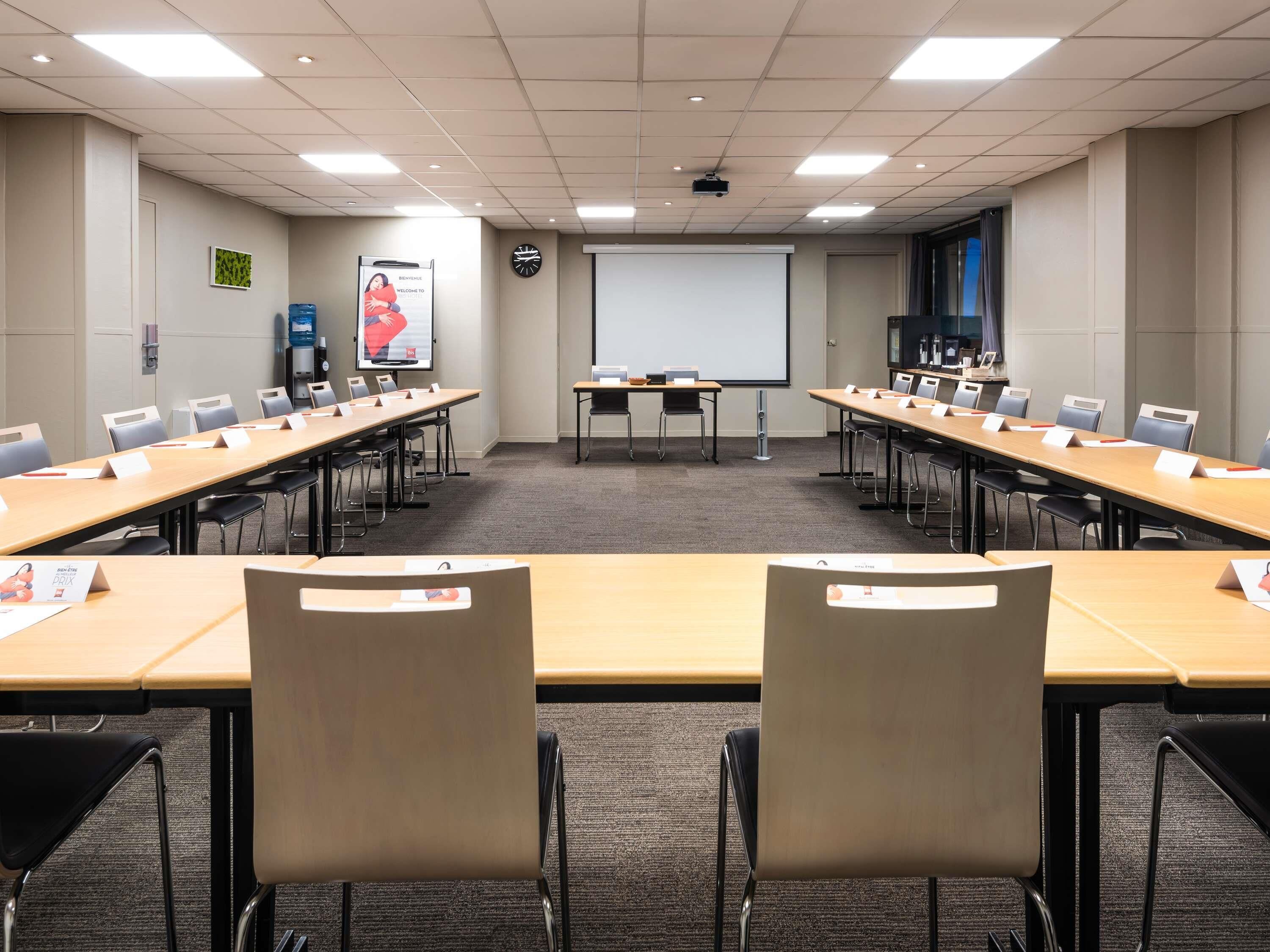 A conference room with long tables, chairs, a projector screen, and a clock on the wall.