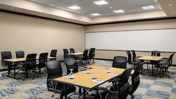 A conference room with a large projection screen, multiple tables, and chairs arranged for meetings.
