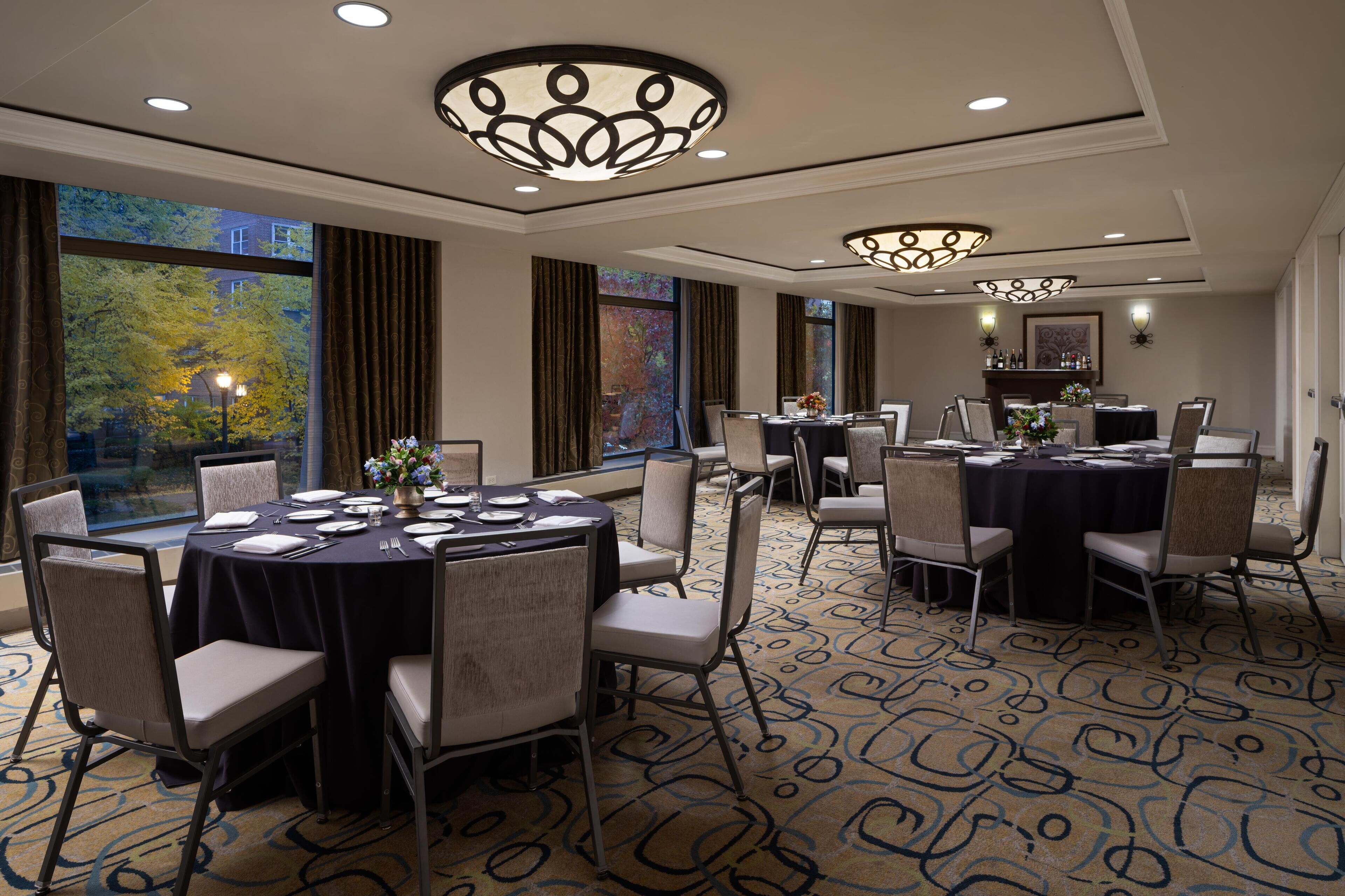 A conference room with round tables, chairs, and a large window with curtains.