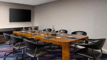 Une salle de conférence avec une longue table, des chaises noires et un téléviseur à écran plat fixé au mur.