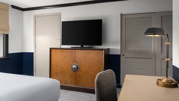 Una habitación de hotel con cama, televisión sobre un mueble de madera, escritorio con lámpara y armario.