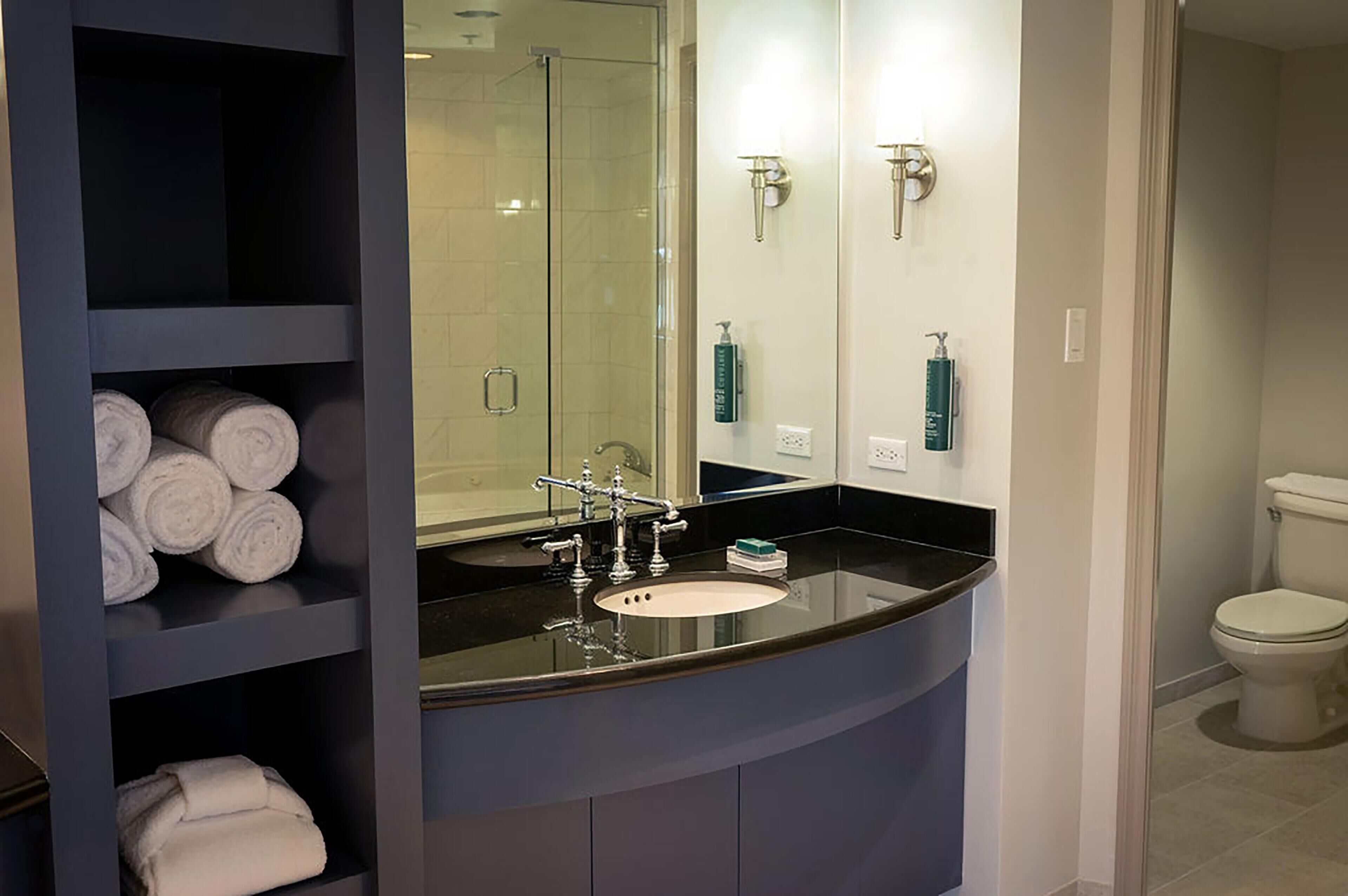 Un baño moderno con lavamanos de encimera negro, ducha con mampara de vidrio y retrete.
