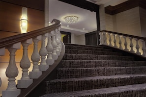 A grand staircase with a wooden handrail and white balusters, leading to a landing with a chandelier. - Hilton Orrington / Evanston (Evanston)